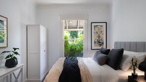 A bedroom with a bed, a window with a view of greenery, a white wardrobe, and a painting on the wall. - Sunshine House-Beautiful refurbished 4 Bedrooms with magnificinet gardens (Daylesford)
