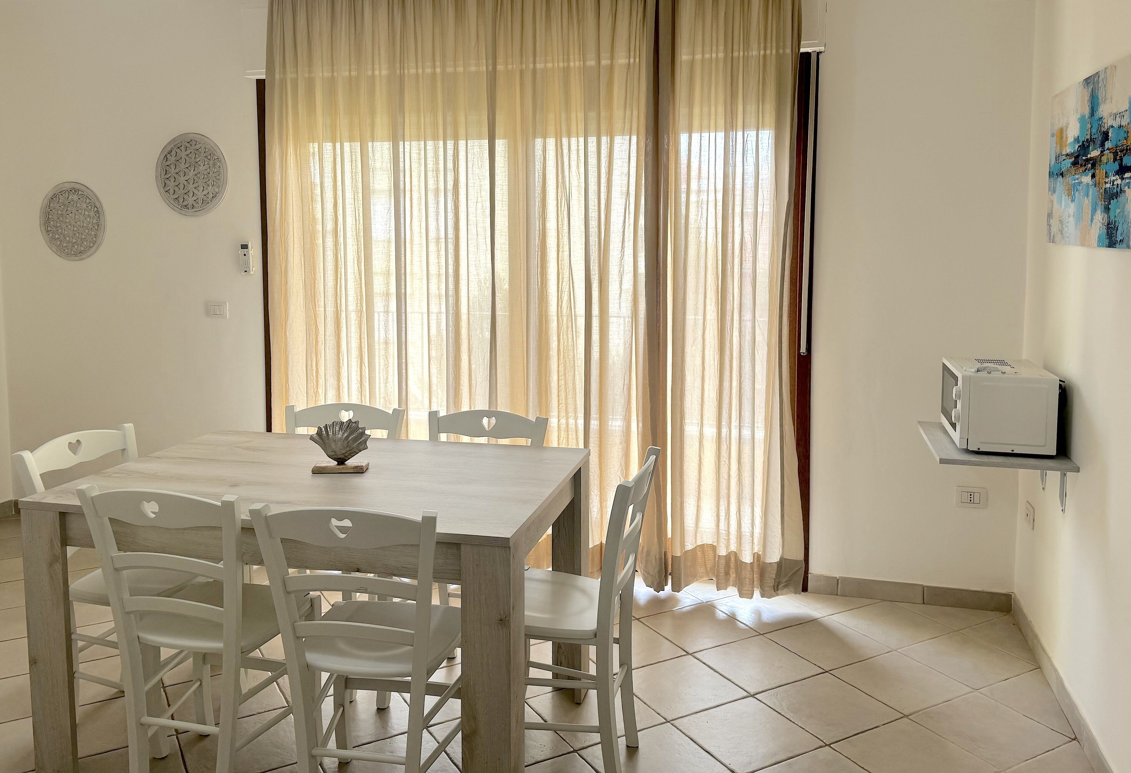 A dining area with a wooden table and white chairs, a small decorative item on the table, and a television on a shelf.