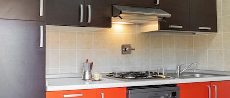 A kitchen with dark brown cabinets, a white countertop, a gas stove, a dishwasher, and a stainless steel sink.