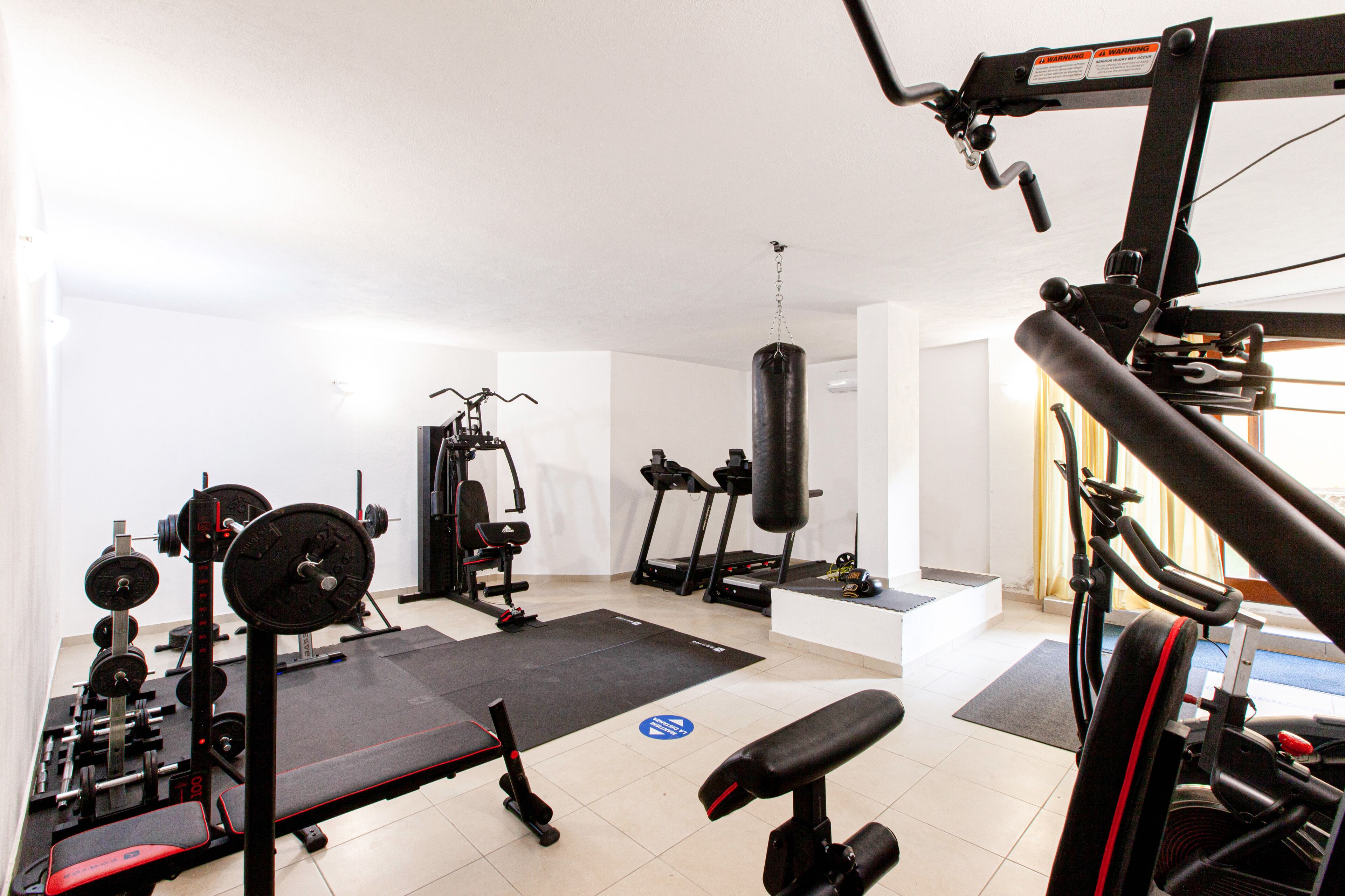 A gym with various exercise equipment including a bench, weight bench, and punching bag.