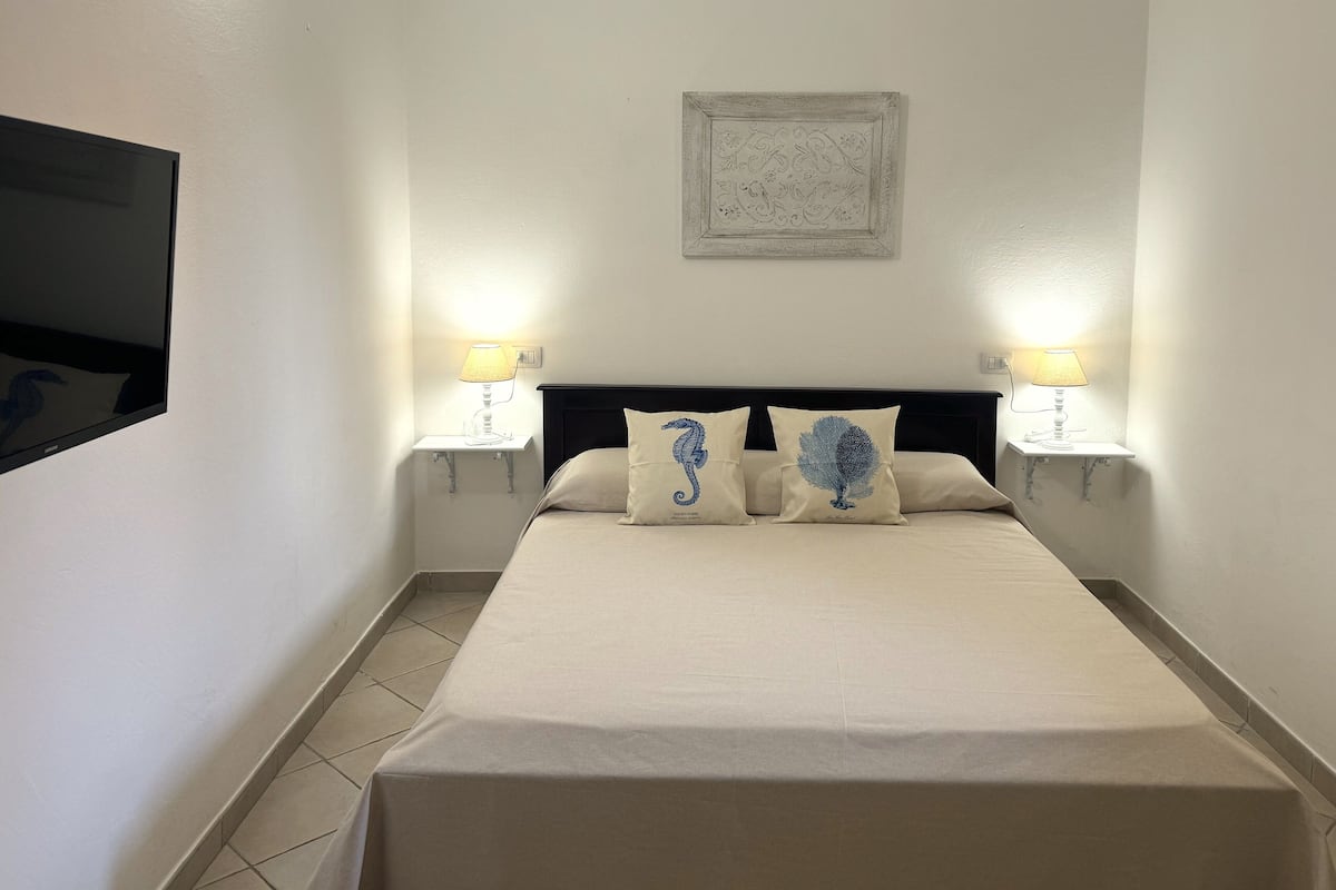 A neatly made bed with a beige bedspread and two decorative pillows, flanked by two bedside lamps on either side.