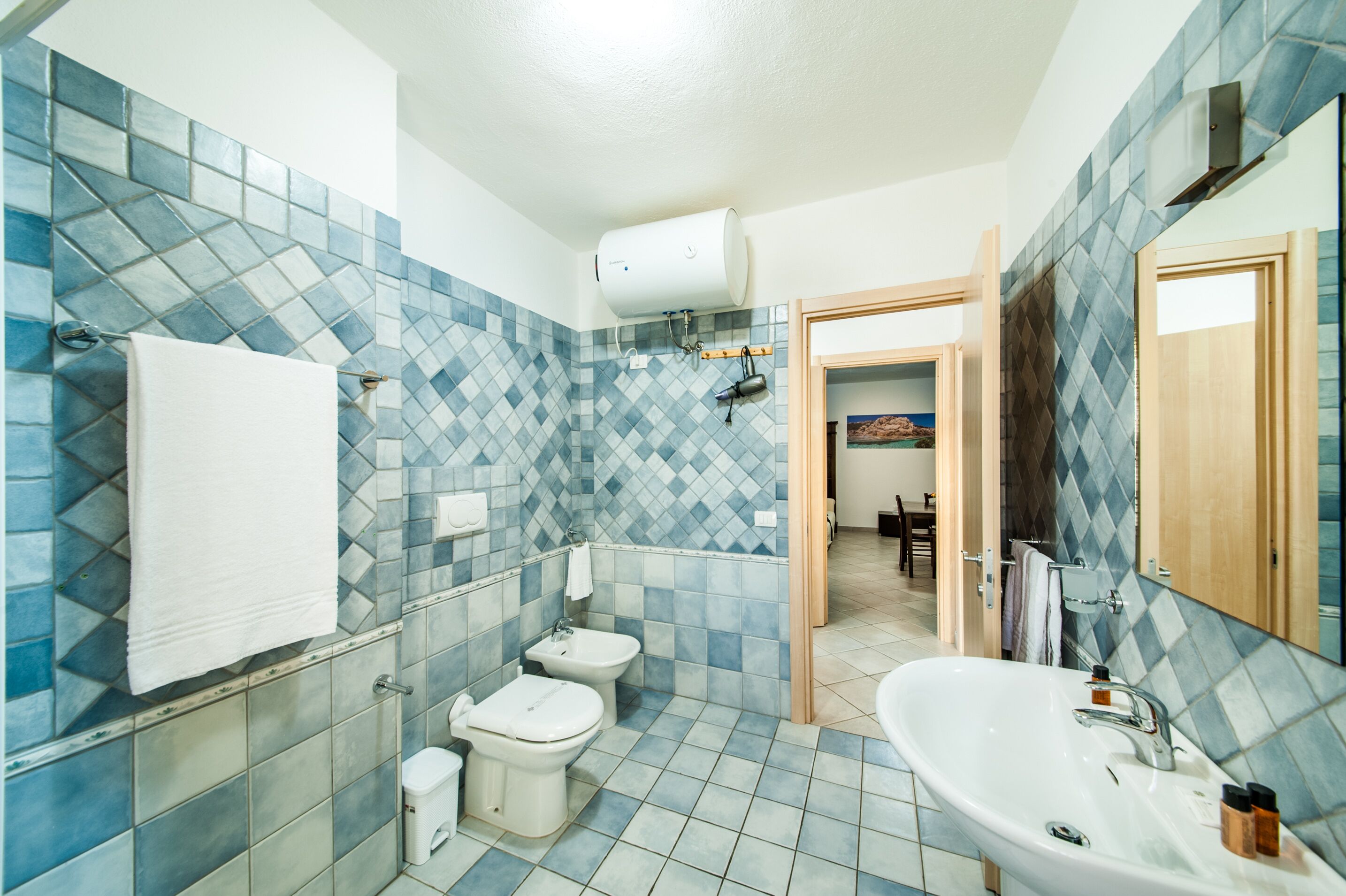A bathroom with a blue-tiled wall, a white sink, and two toilets.