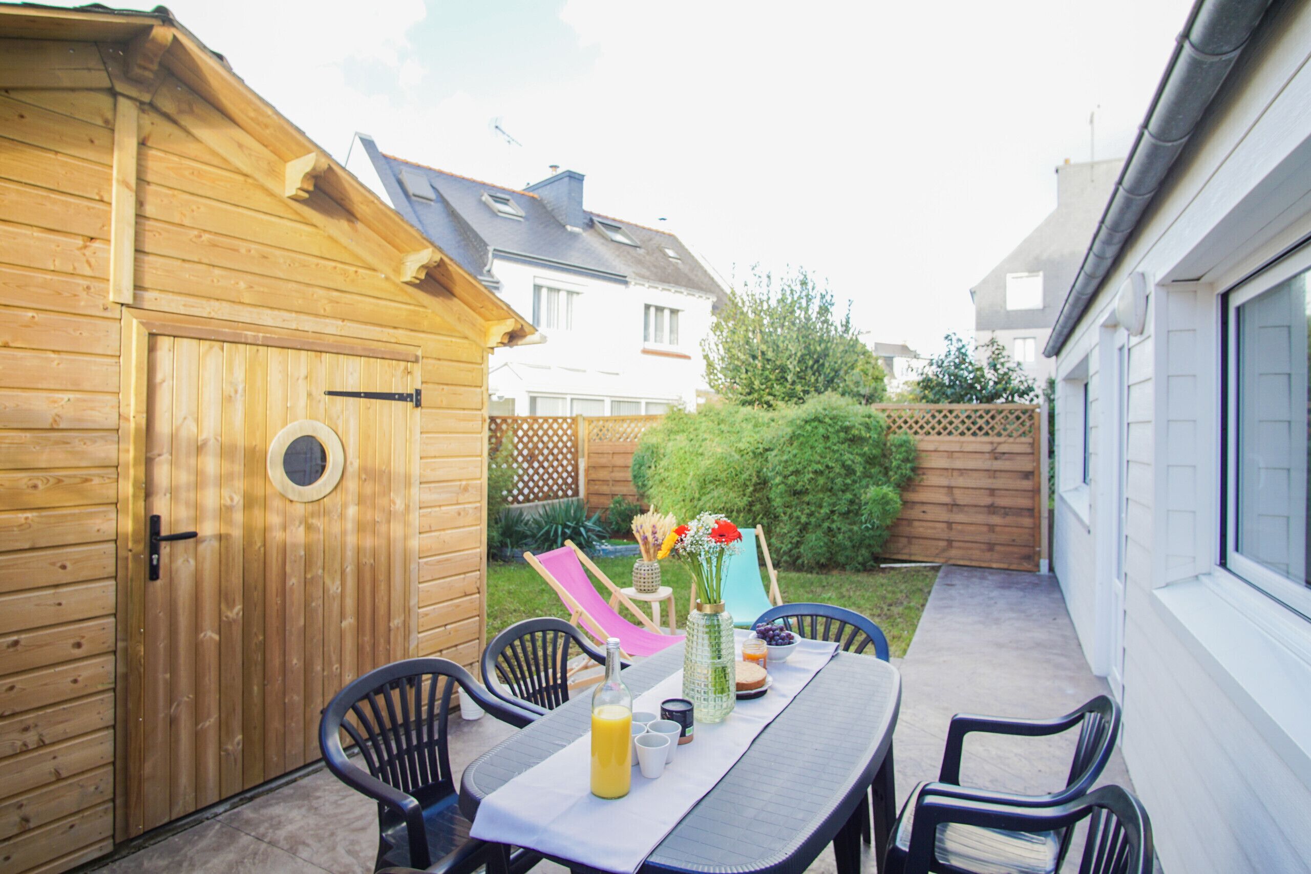 A wooden deck with a table set for two, surrounded by chairs, and a wooden shed in the background.