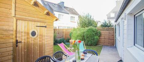 A wooden deck with a table set for two, surrounded by chairs, and a wooden shed in the background.