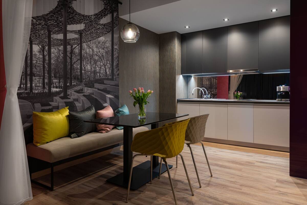 A modern kitchen with dark cabinetry, a glass-top dining table, and a yellow chair.