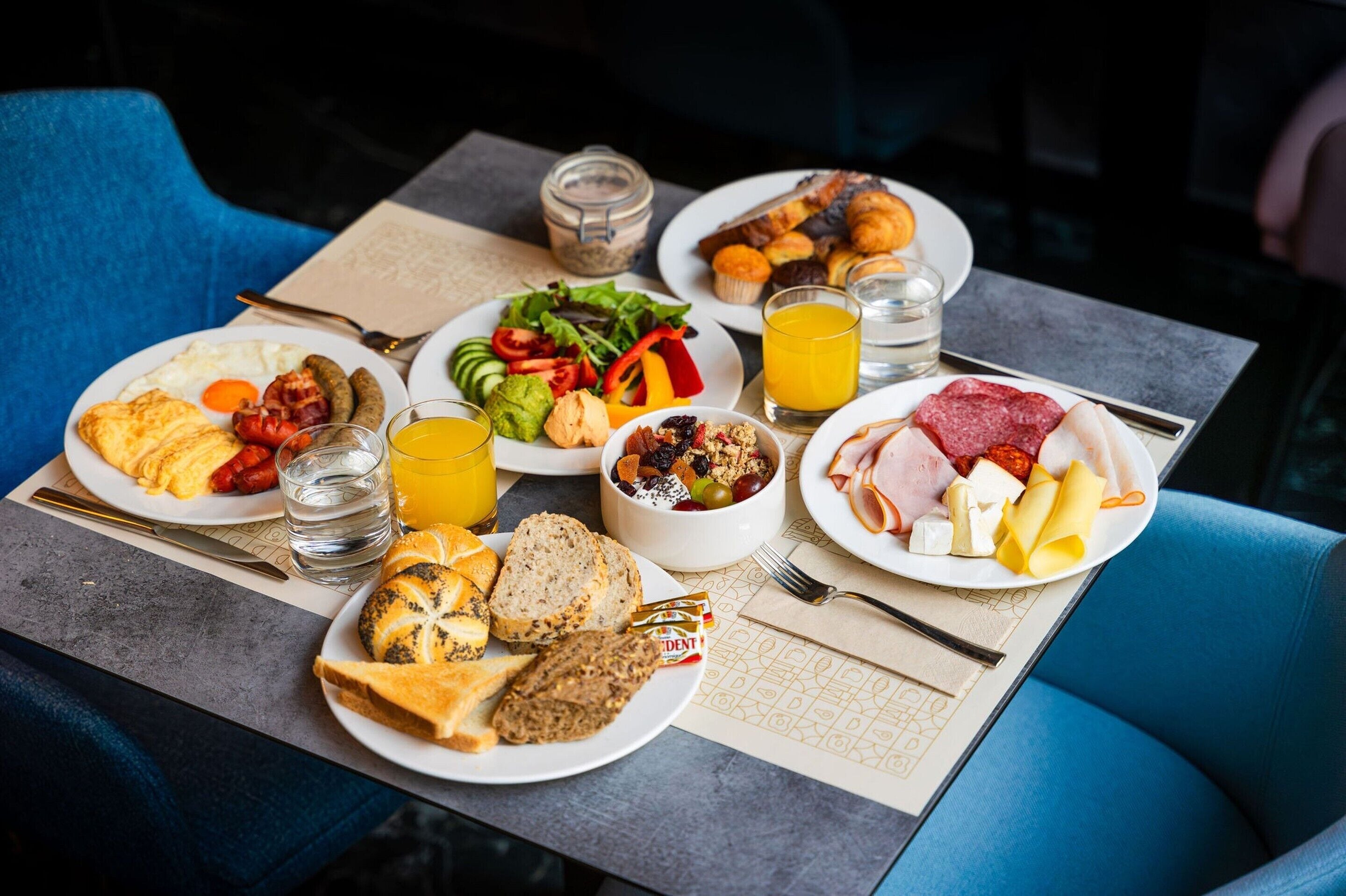 A breakfast table with various dishes, including eggs, sausages, toast, and a fruit bowl.