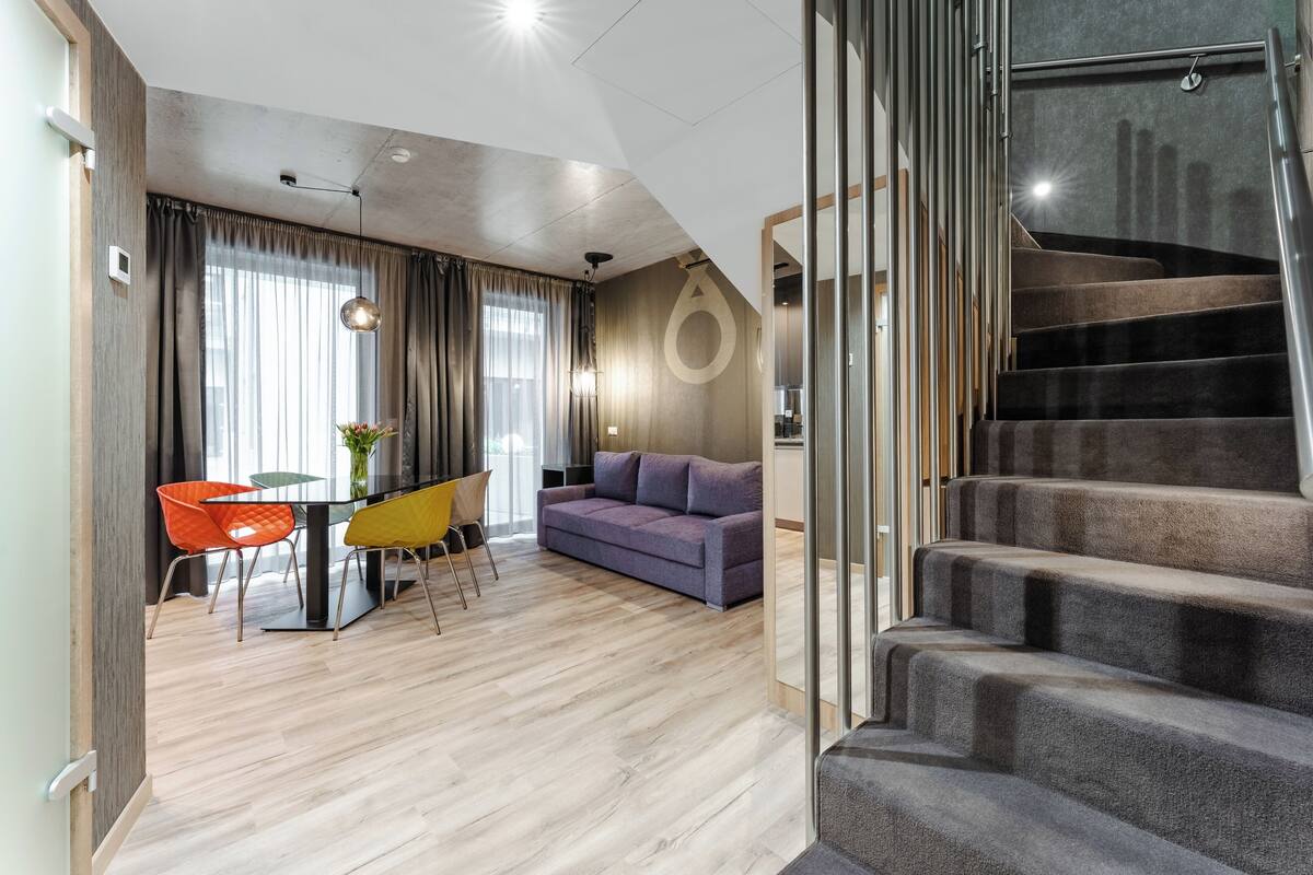 A modern living room with a sofa, dining table, chairs, and a staircase.