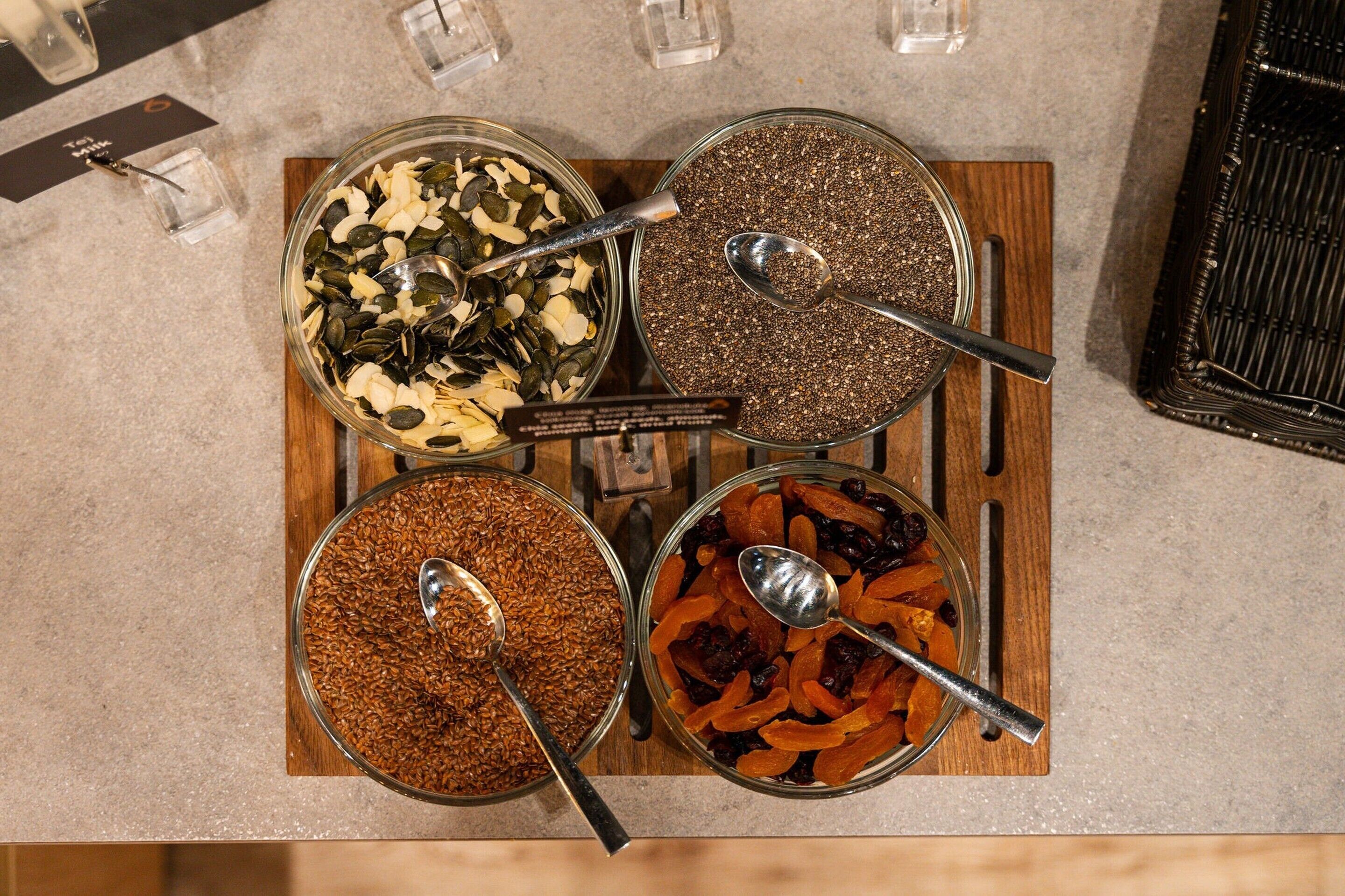 Four glass containers with different food items on a wooden board.
