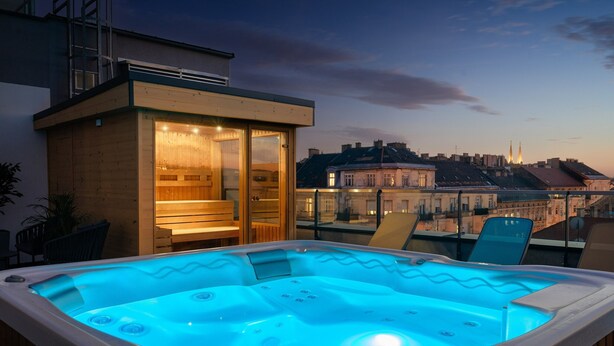 A hot tub with a wooden exterior and glass doors, overlooking a cityscape with buildings and a church spire. - Onyx Luxury Budapest (Budapest)