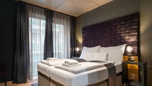 A modern hotel room with a large bed, a nightstand with a lamp, and a view through sheer curtains. - Onyx Luxury Budapest (Budapest)