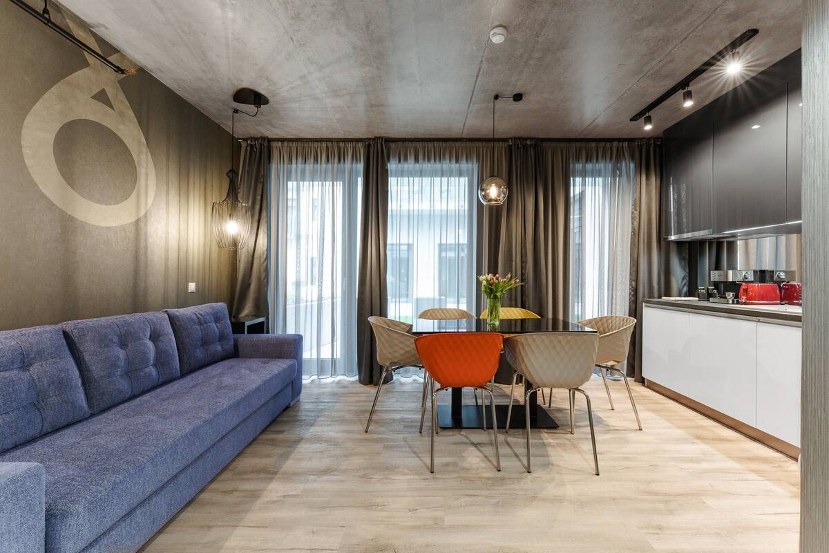 A modern living room with a sofa, dining table, chairs, and a kitchen area with cabinets and appliances.