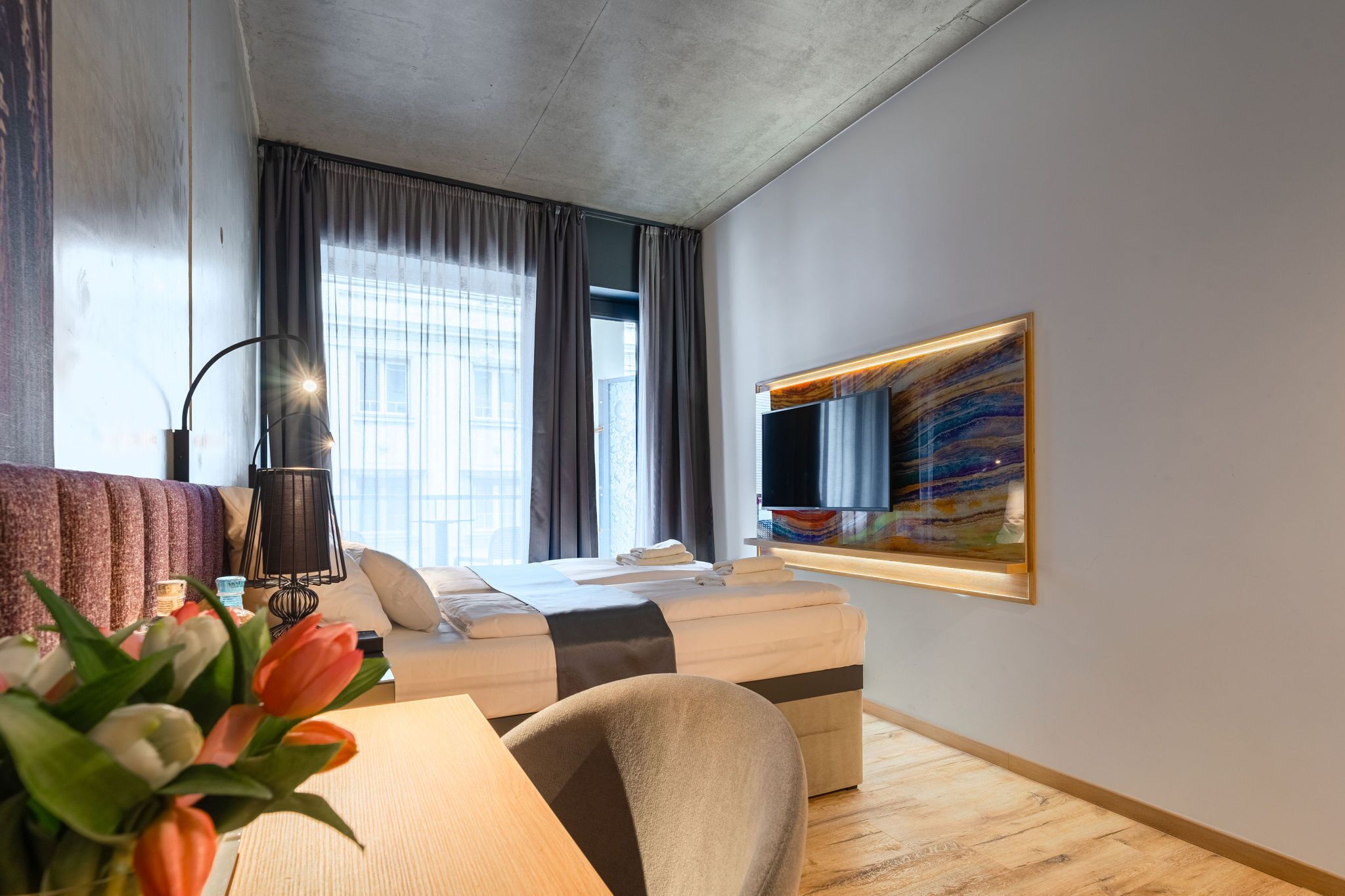 A modern hotel room with a sofa, a desk, a chair, a bed, a TV, and a painting on the wall.