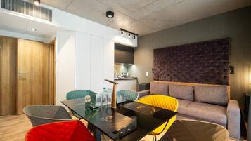 Una sala de estar moderna con un sofá, una mesa de comedor y sillas. Se observa un área de cocina al fondo.
