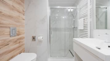 Un baño moderno con pared de madera, cabina de ducha de vidrio y tocador blanco con espejo.