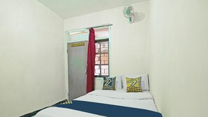 A small, simple room with a bed, a window with a red curtain, and a wall-mounted fan. - SPOT ON 91545 Pondok Mukti Syariah (Bandung)