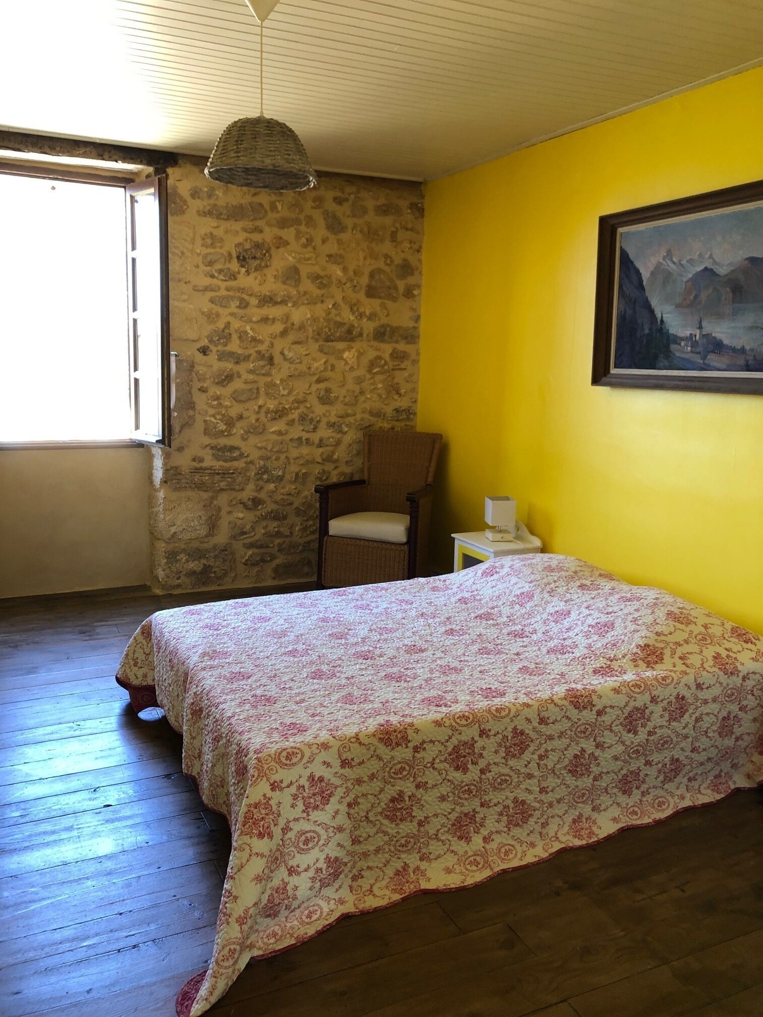 Une chambre à coucher avec un lit, une chaise, une table de chevet, un tableau et un mur en pierre.