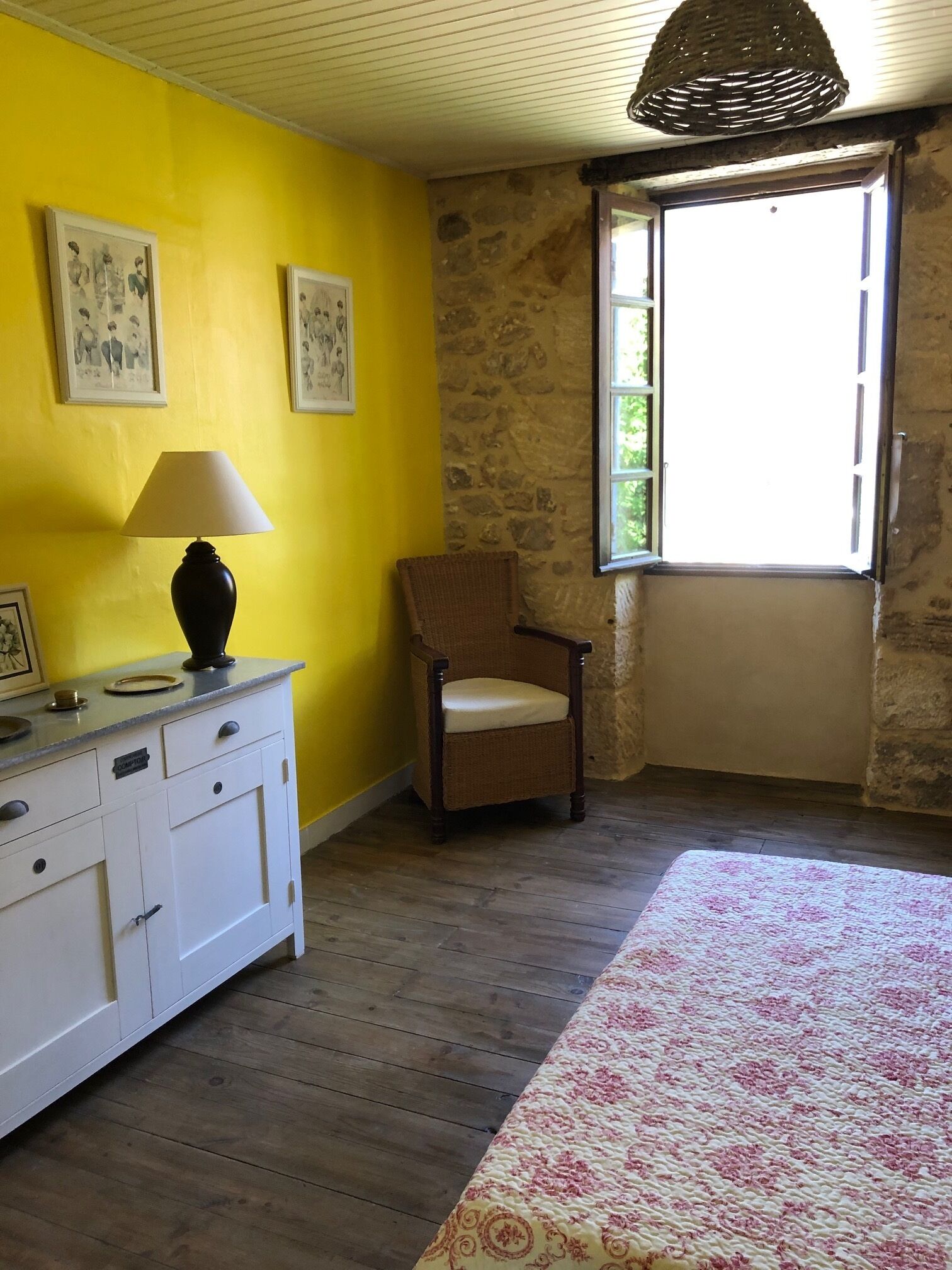 A room with a yellow wall, a stone wall, a window, a chair, a bed, and a dresser.