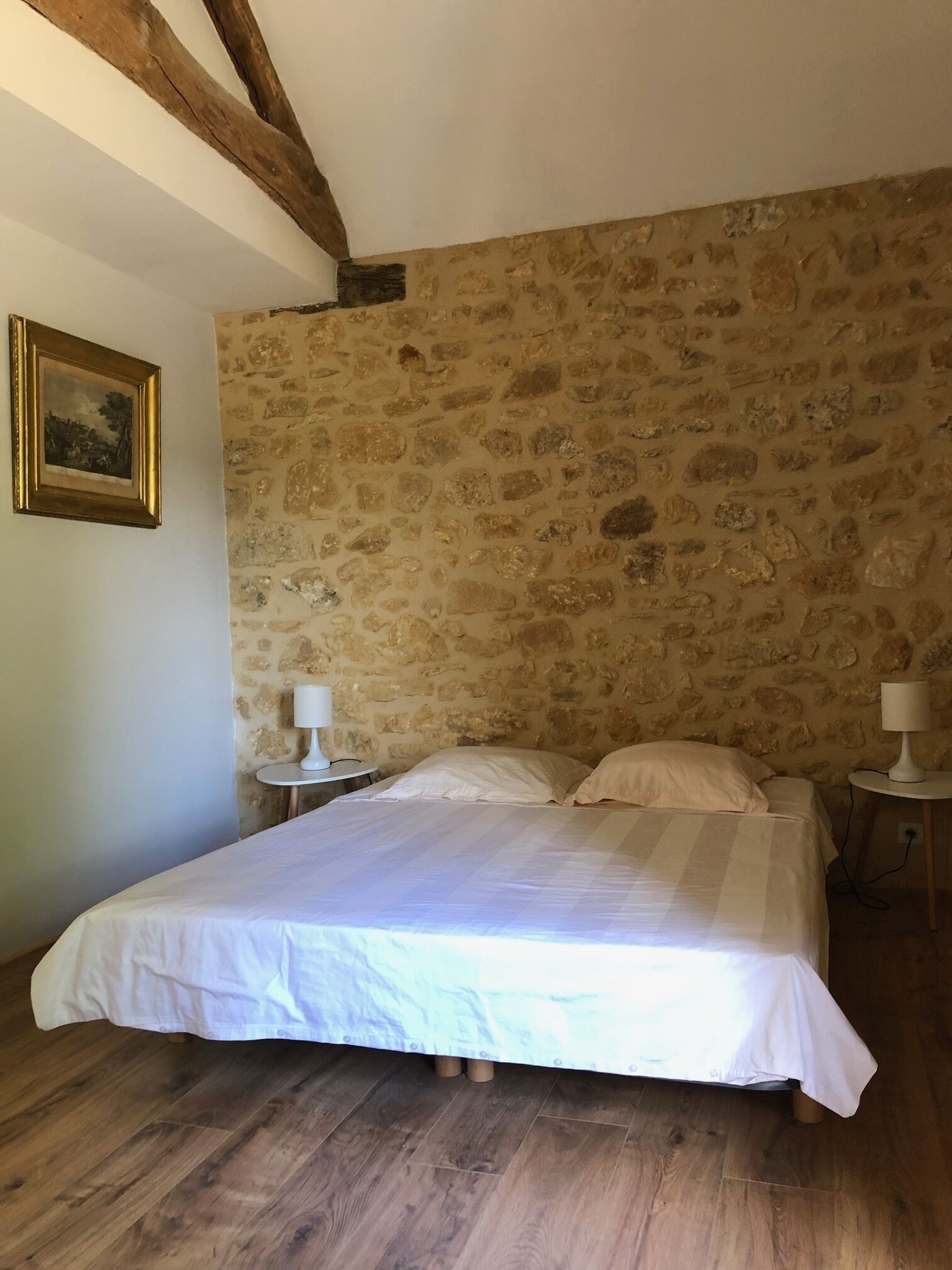 Ein Schlafzimmer mit Steinwand, einem Bett mit weißer Bettwäsche, zwei Nachttischen mit Lampen und einem gerahmten Bild an der Wand.