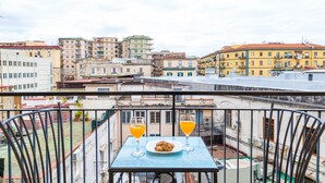 Un balcon avec une table préparée pour le petit-déjeuner, offrant une vue sur un paysage urbain composé de différents bâtiments.