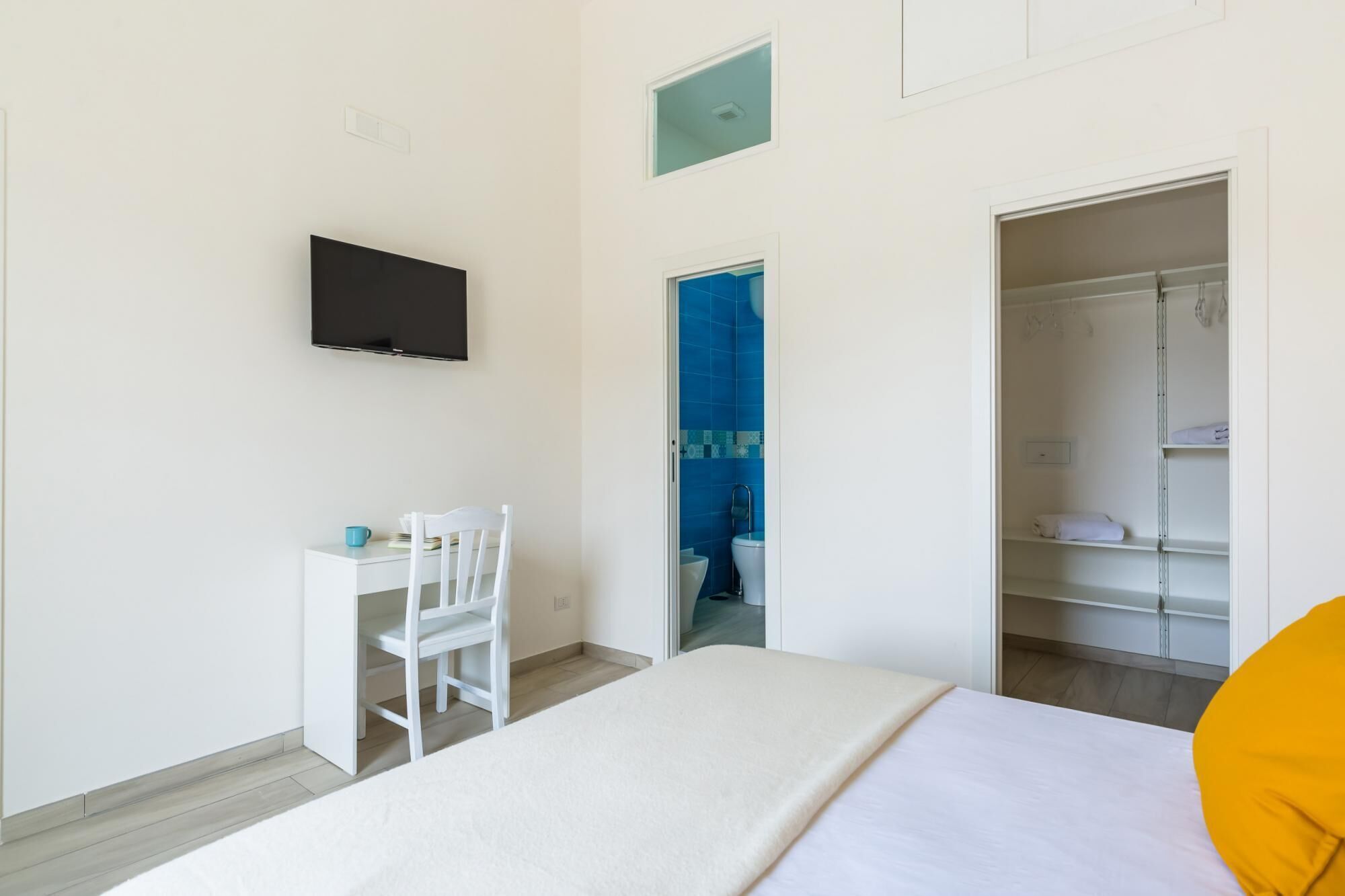 A bedroom with a bed, a desk, a chair, a TV, a wardrobe, and a bathroom with blue tiles.