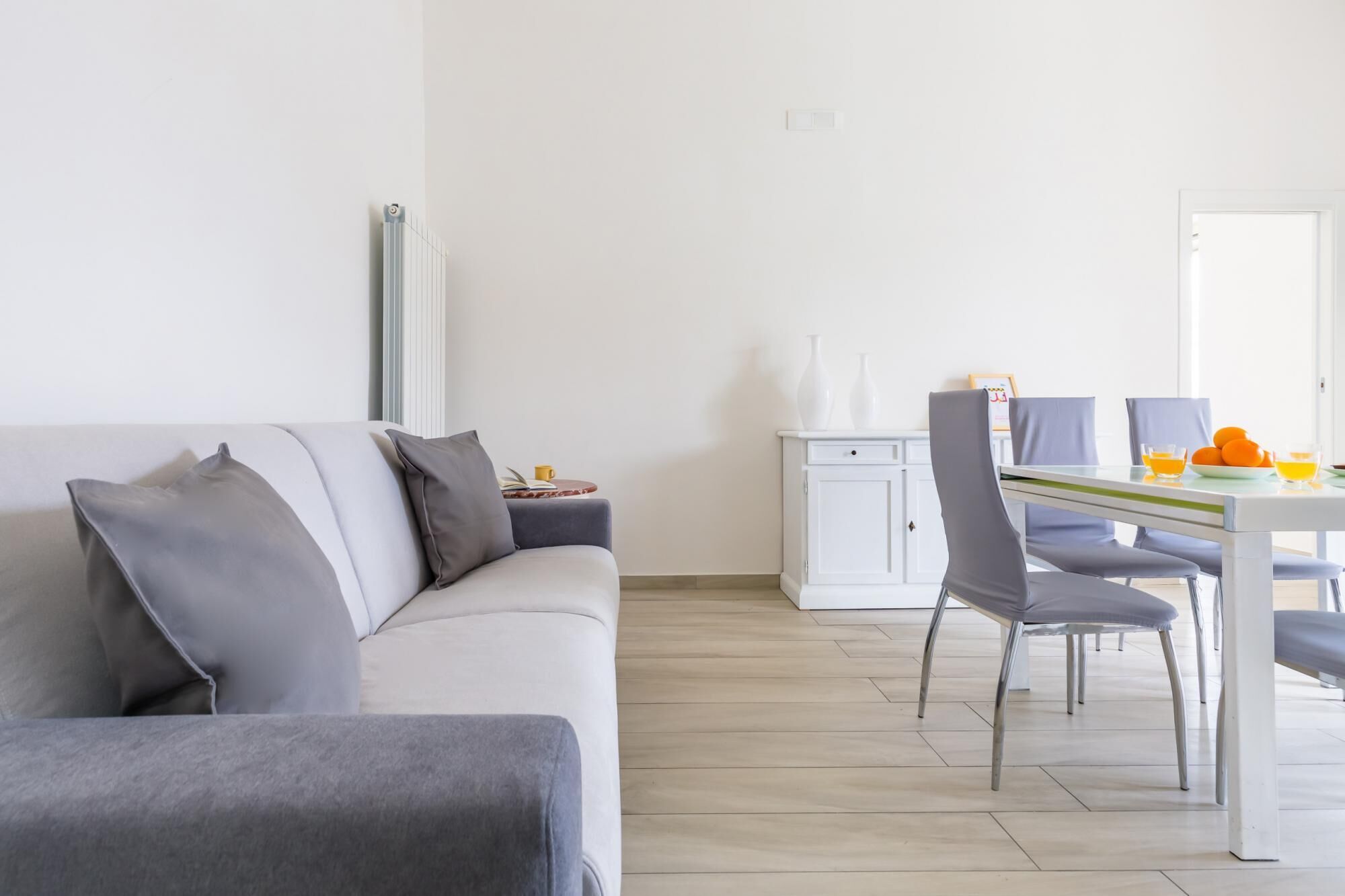 A modern living room with a grey sofa, a dining table with chairs, and a white cabinet.