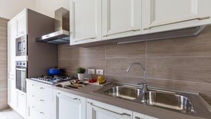 Une cuisine moderne avec des meubles blancs, un évier en acier inoxydable, une casserole bleue et une cuisinière à gaz.