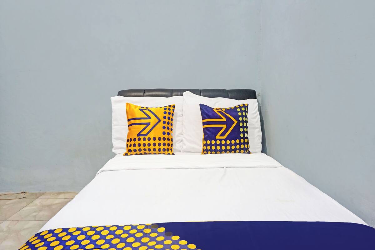 Una cama con dos almohadas mostrando un diseño geométrico, un edredón blanco y una manta de lunares azules y amarillos.