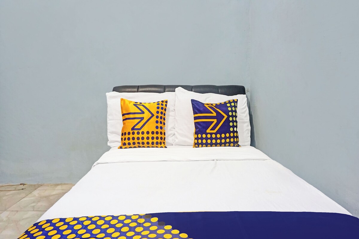 Ein Bett mit zwei Kissen, einem geometrischen Muster, einer weißen Bettdecke und einer Decke mit blauen und gelben Punkten.
