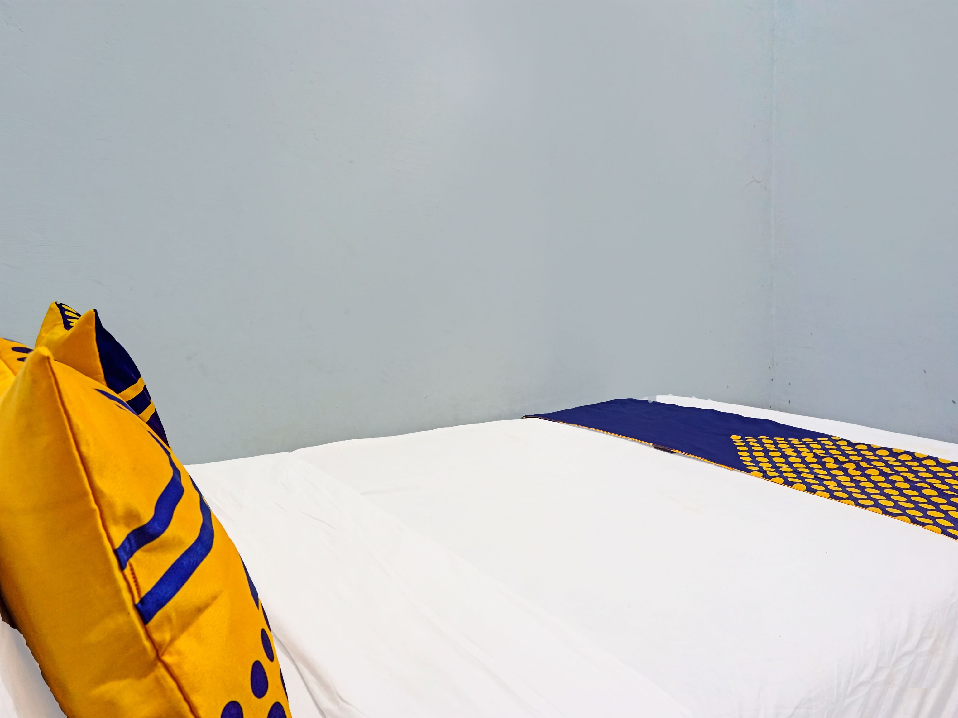Un lit avec une literie blanche et une couverture à motifs bleus et jaunes.