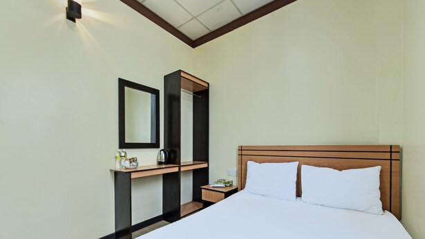 A hotel room with a bed, a nightstand, a mirror, and a small table with a kettle and a bottle. - SPOT ON 91723 Sony Homestay Syariah (Sukabumi)
