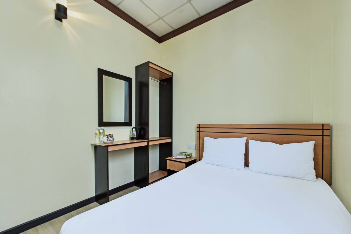 Een hotelkamer met een bed, een nachtkastje, een spiegel en een klein tafeltje met een waterkoker en een fles.