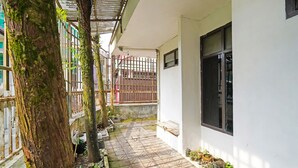 A narrow, covered outdoor corridor with a tiled floor, a white wall with a window, and a metal gate. - SPOT ON 91723 Sony Homestay Syariah (Sukabumi)