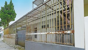 A building with a metal fence and barred windows, a concrete pathway, and a tree in the background. - SPOT ON 91723 Sony Homestay Syariah (Sukabumi)