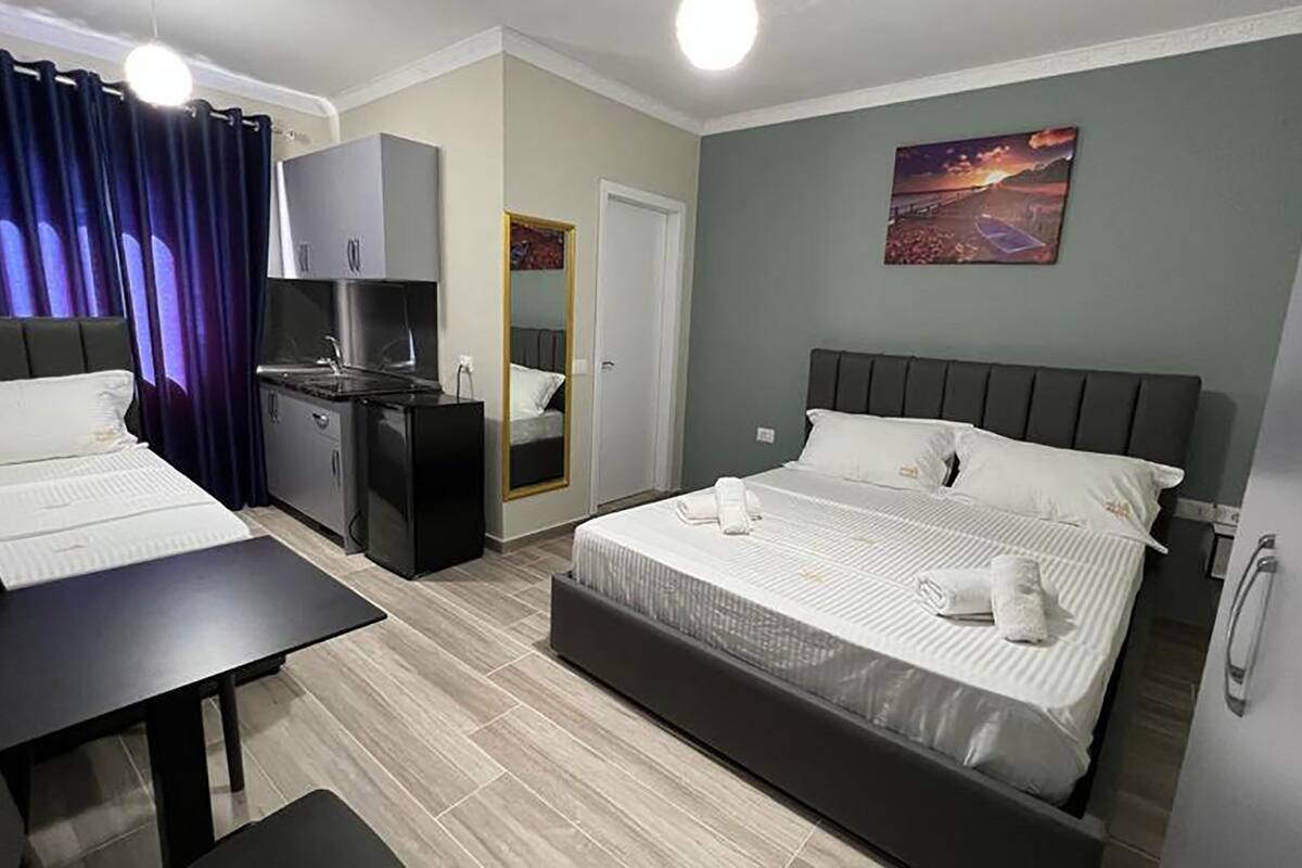 A hotel room with two beds, a desk, a kitchenette, and a bathroom.