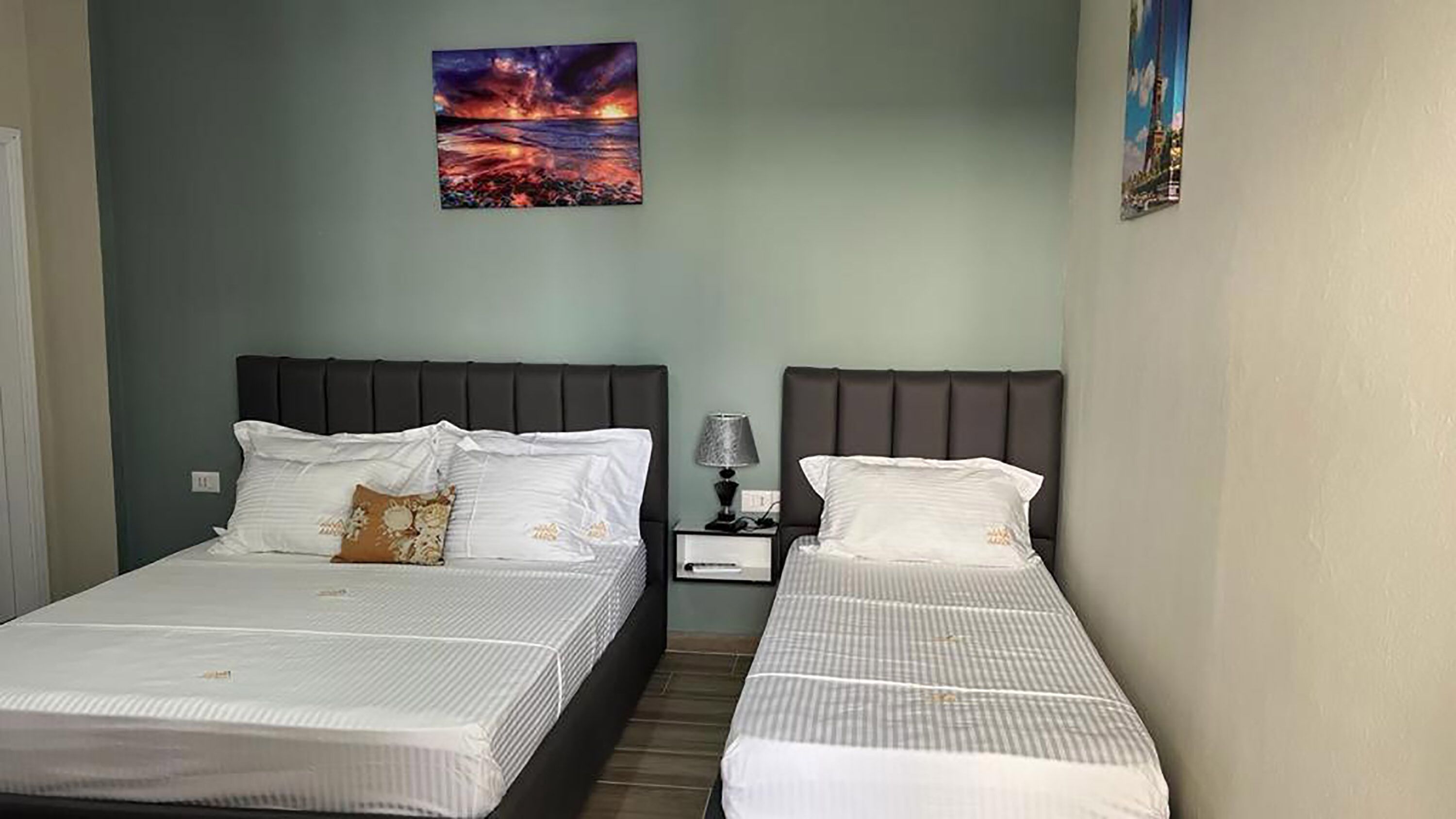 A hotel room with two beds, a nightstand with a lamp, and a painting on the wall.