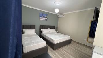 A bedroom with two beds, a ceiling fan, a painting on the wall, and a window with curtains.