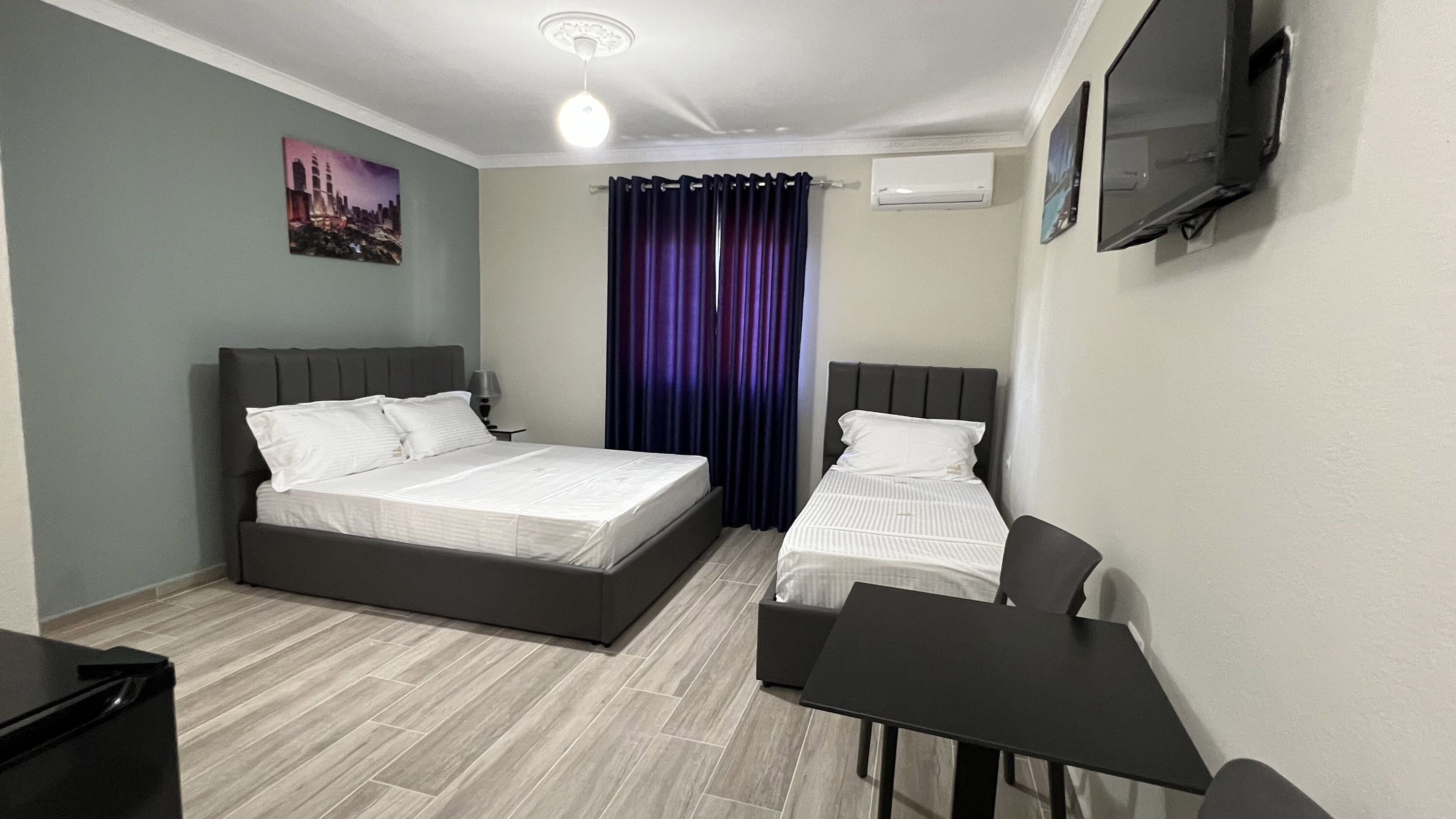 Una habitación de hotel con cama, escritorio, silla, televisor y ventana con cortinas.