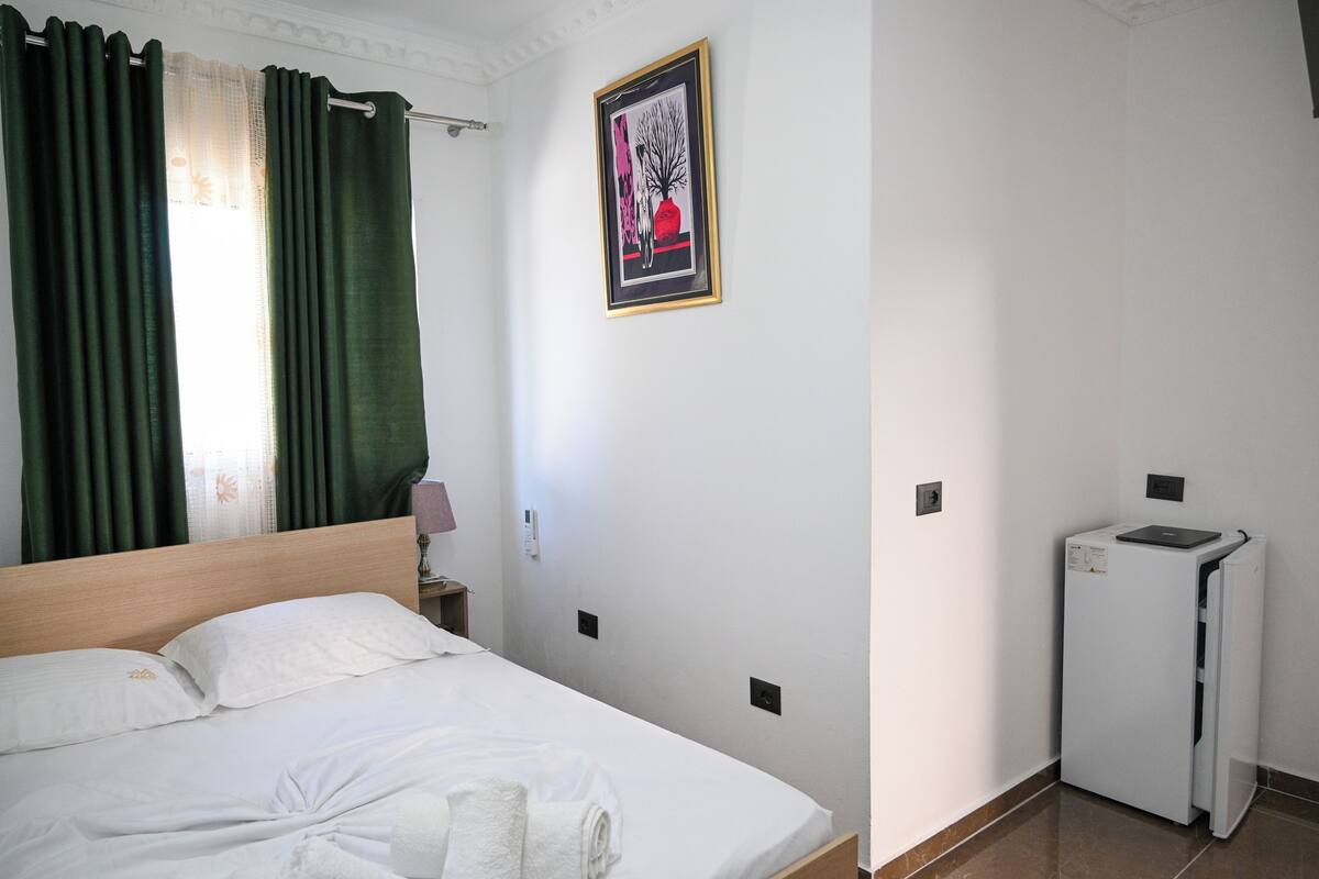 A hotel room with a bed, a wall-mounted picture, and a small refrigerator.
