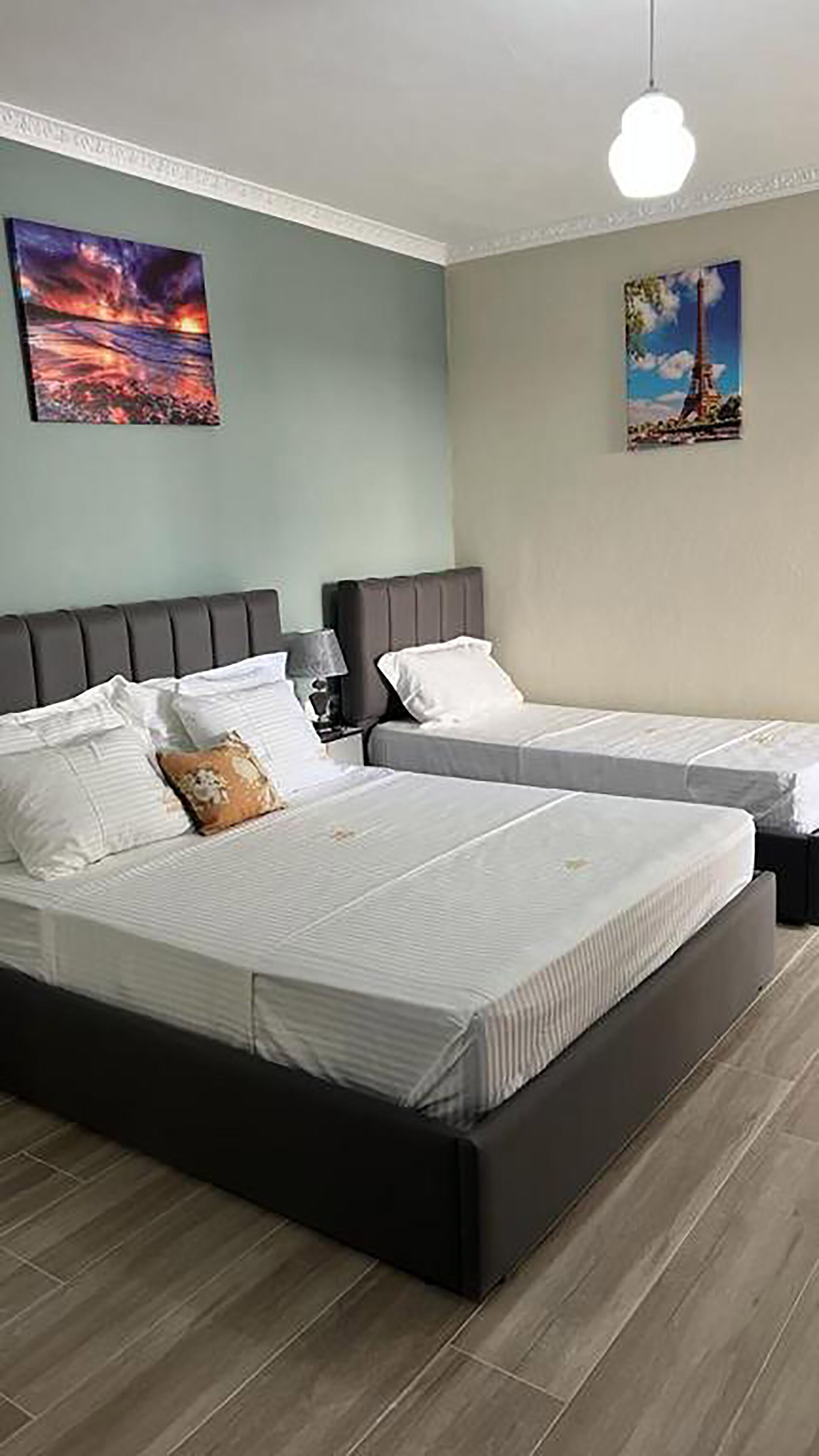 A bedroom with two beds, a nightstand, a lamp, and two wall art pieces.