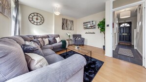 A modern living room with a sectional sofa, a coffee table, and a TV. There is a clock on the wall and a plant in the corner.