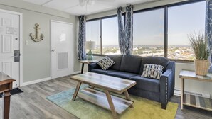Un salon moderne avec un canapé, une table basse et une vue sur la ville grâce à de grandes fenêtres.