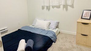 A bedroom with a bed, a bedside table, a window with sheer curtains, and a framed picture on the wall. - Centrally located, Cozy two bedroom basement apartment, 10 mins from YYC airport (Calgary)