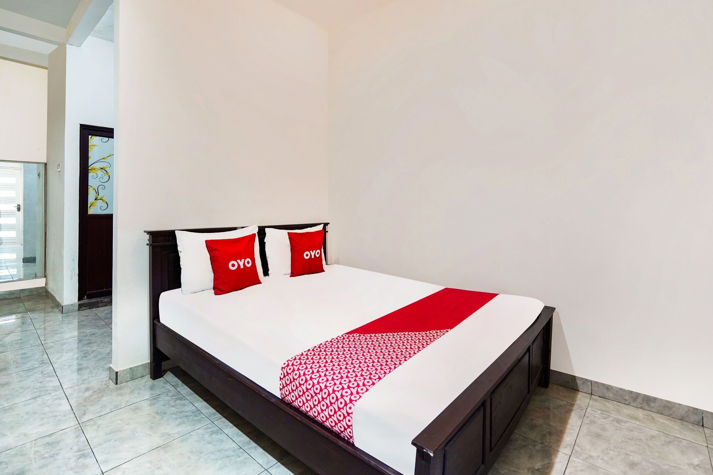 Una cama bien tendida con una colcha roja y blanca y dos almohadas rojas con el logotipo 'OYO'.