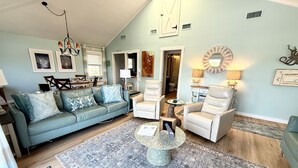 A living room with a blue sofa, two white armchairs, a coffee table, and a patterned rug.