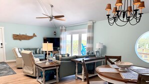 A living room with a sofa, chairs, a dining table, a chandelier, and a ceiling fan.