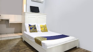 A single bed with white bedding, two pillows with yellow and blue patterns, a white headboard, and an air conditioning unit above. - SPOT ON 91765 Kaiku Guest House (Tasikmalaya)
