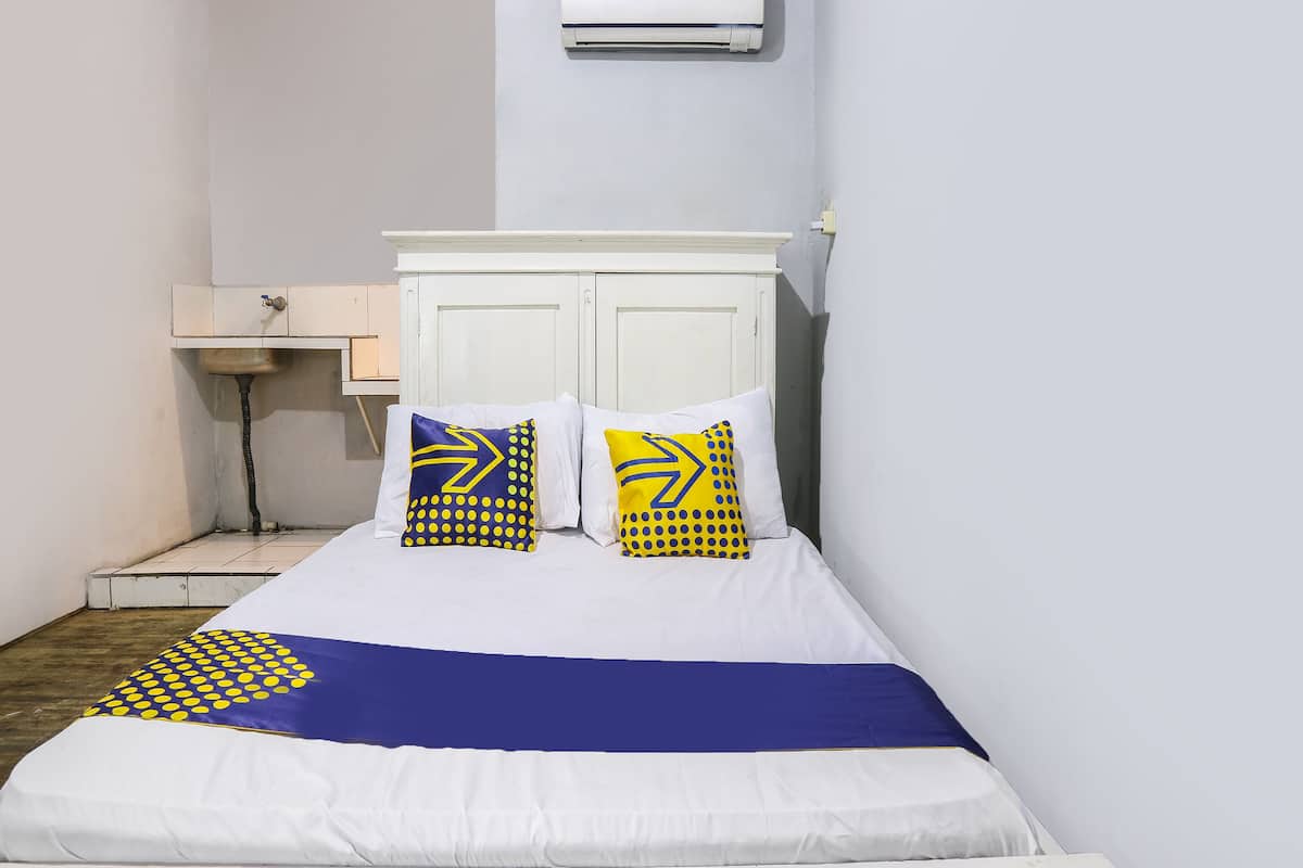 Un lit avec une literie blanche, deux oreillers aux motifs jaunes et bleus, une tête de lit blanche et un appareil de climatisation placé au-dessus.