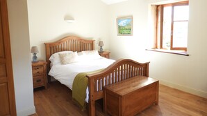 Un dormitorio con una cama de madera, una mesita de noche con lámparas, un banco y una ventana con vistas.