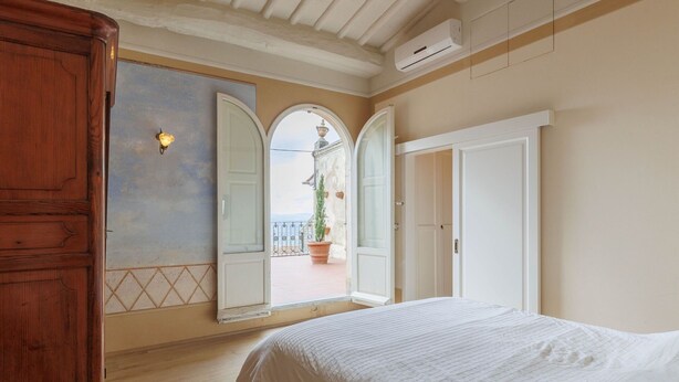 A bedroom with a bed, a wooden wardrobe, and a large mirror. - Beautiful apartment for 4 people with WIFI, A/C, terrace and panoramic view (Cortona)