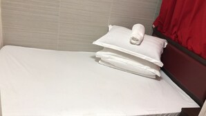Un lit bien fait, avec du linge de lit blanc et des oreillers, une tête de lit en bois et un rideau rouge.